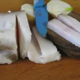 Smalec gęsi na stawy, pokrojony w plastry, leży obok chleba i cebuli.