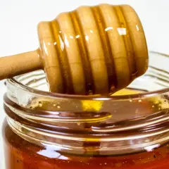 Drewniana chochla zanurzona w słoiku z miodem, który może być naturalnym antybiotykiem na stawy.
