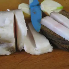 Smalec gęsi na stawy, pokrojony w plastry, leży obok chleba i cebuli.