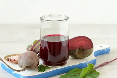 Szklanka z sokiem z buraka, obok całe i przekrojone buraki, liście i przyprawy. Pomyśl o zdrowych tabletkach z buraka.