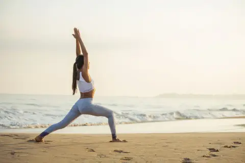 Kobieta w pozycji wojownika na plaży o wschodzie słońca.