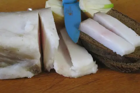 Smalec gęsi na stawy, pokrojony w plastry, leży obok chleba i cebuli.