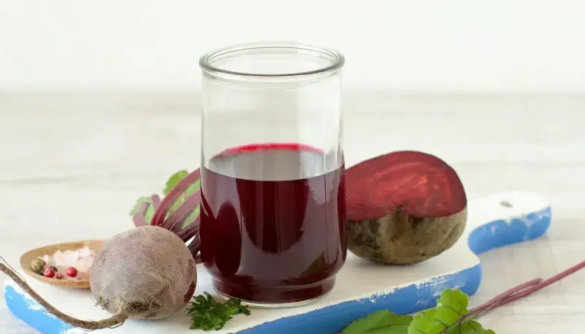 Szklanka z sokiem z buraka, obok całe i przekrojone buraki, liście i przyprawy. Pomyśl o zdrowych tabletkach z buraka.
