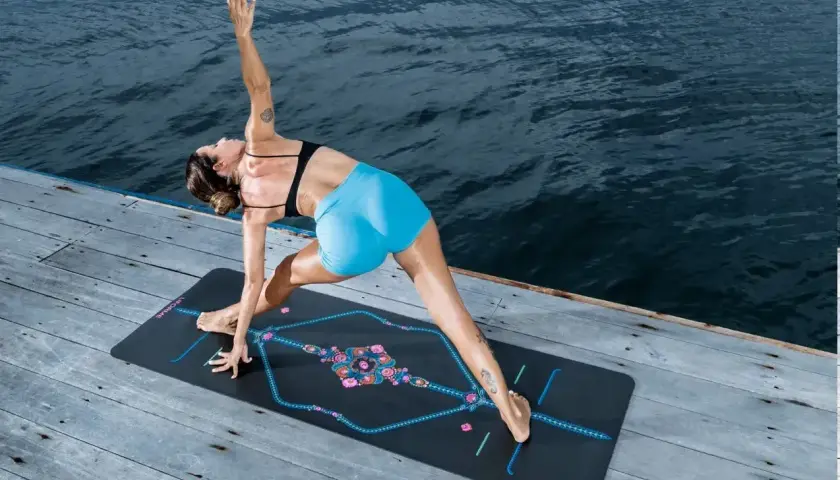 Kobieta w pozie jogi na macie nad wodą, ćwicząca asanę. Stanowi to idealne tło do praktyki yoga nidra.
