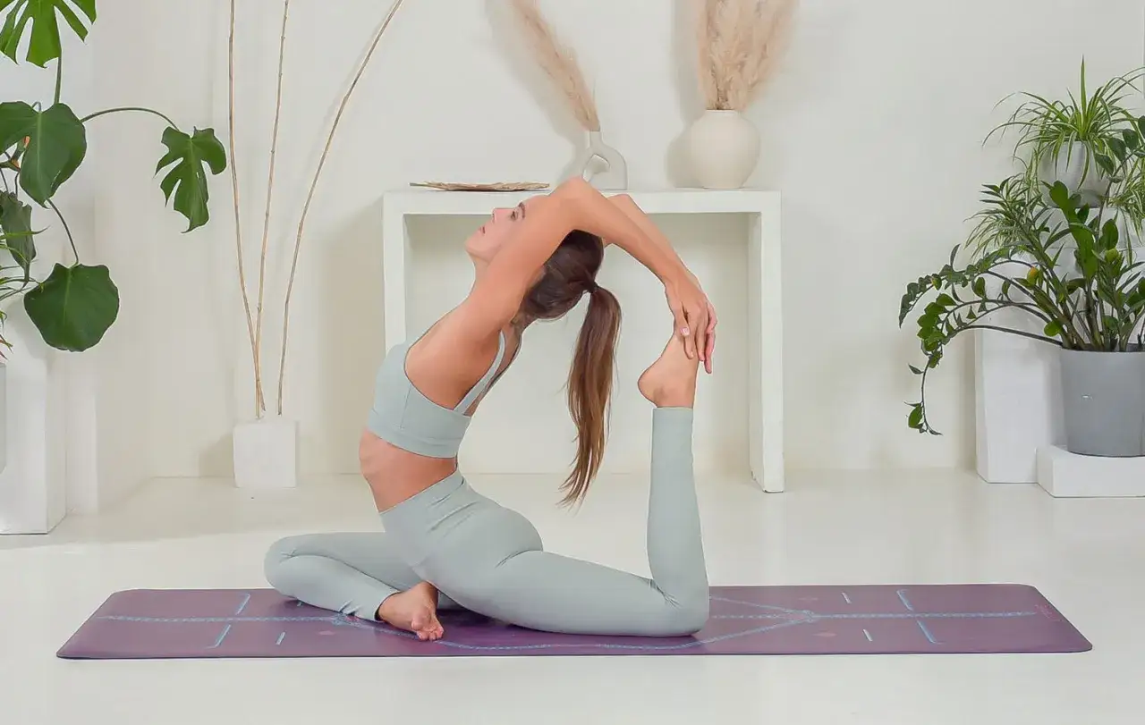 Kobieta w pozycji eka pada rajakapotasana, zgięta w łuk, chwyta stopę.