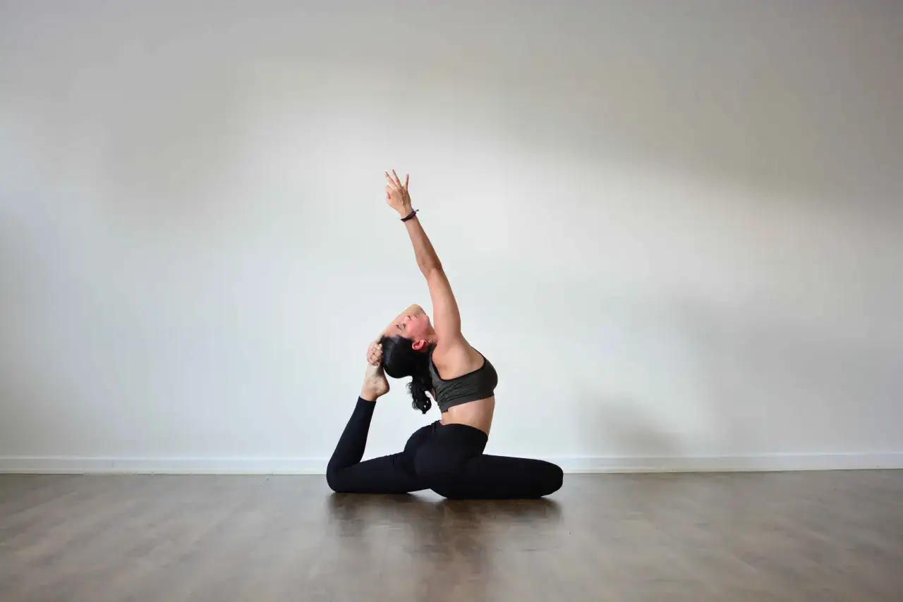 Kobieta w pozycji eka pada rajakapotasana, z ręką wyciągniętą do góry i chwytającą stopę.