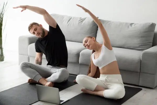 Para ćwiczy jogę w pozycji sukhasana, wykonując skłony boczne, patrząc na laptopa.